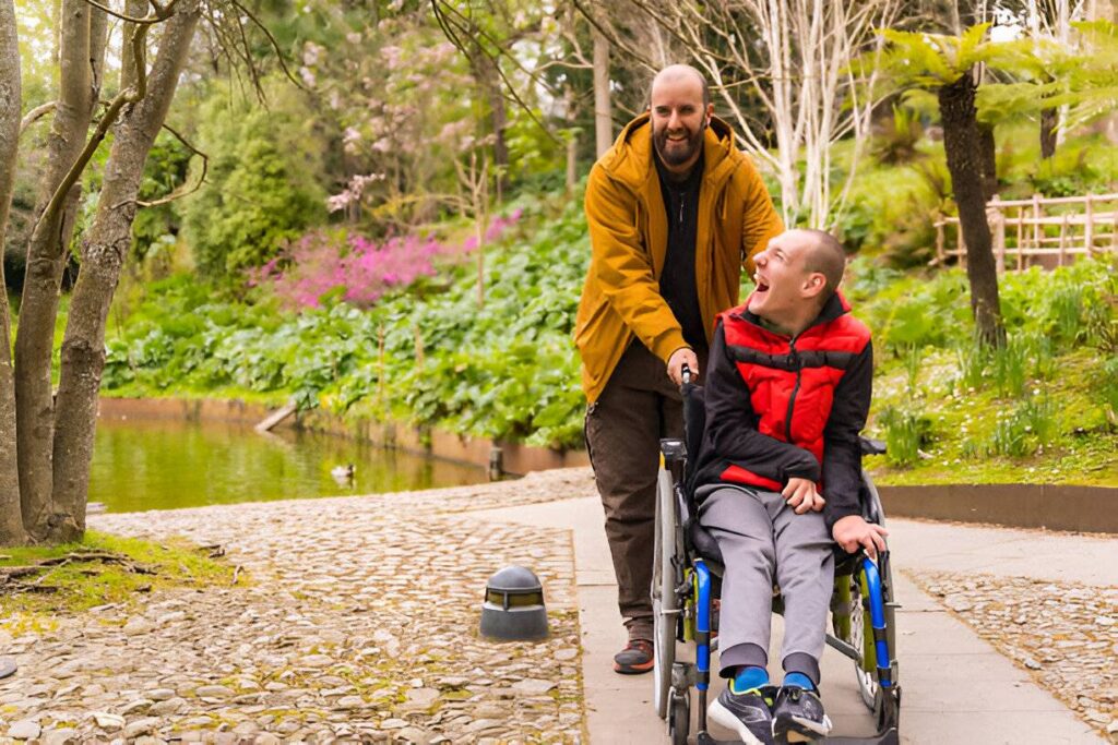 A male support workr assisting a happy young adults with disabilities in wheelchair by Saha Supports